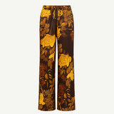 Veranera Pants: wide-leg silk twill trousers with a drawstring waist, featuring a brown and yellow floral print and overlapping script text.