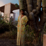 Model wearing a KABE SHOP INC long wrap dress with yellow floral sari-inspired embroidery in a desert landscape.