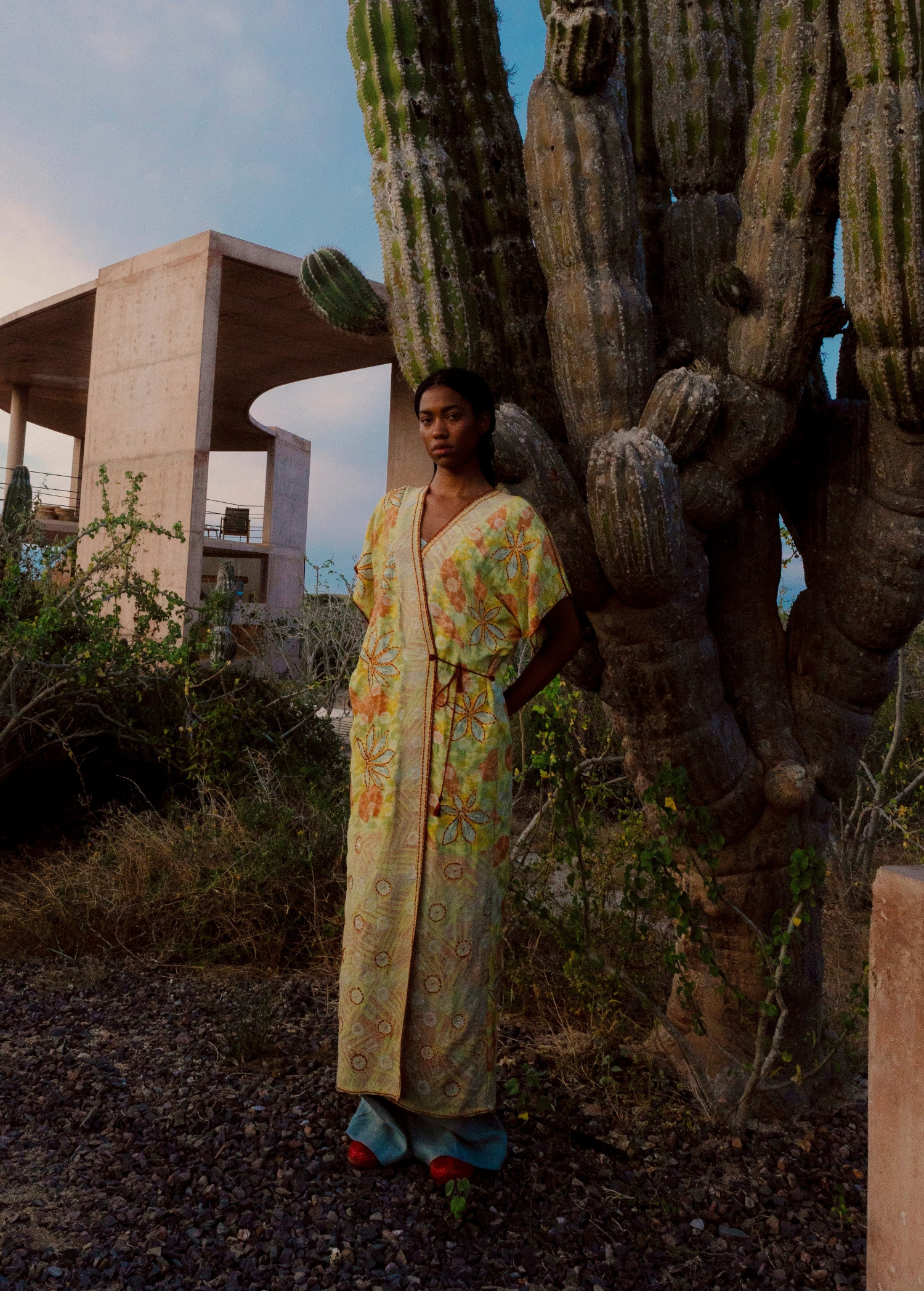 Model wearing a KABE SHOP INC long wrap dress with yellow floral sari-inspired embroidery in a desert landscape.