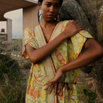 Model wearing a KABE SHOP INC long wrap dress with yellow and green floral sari-inspired embroidery near a cactus.