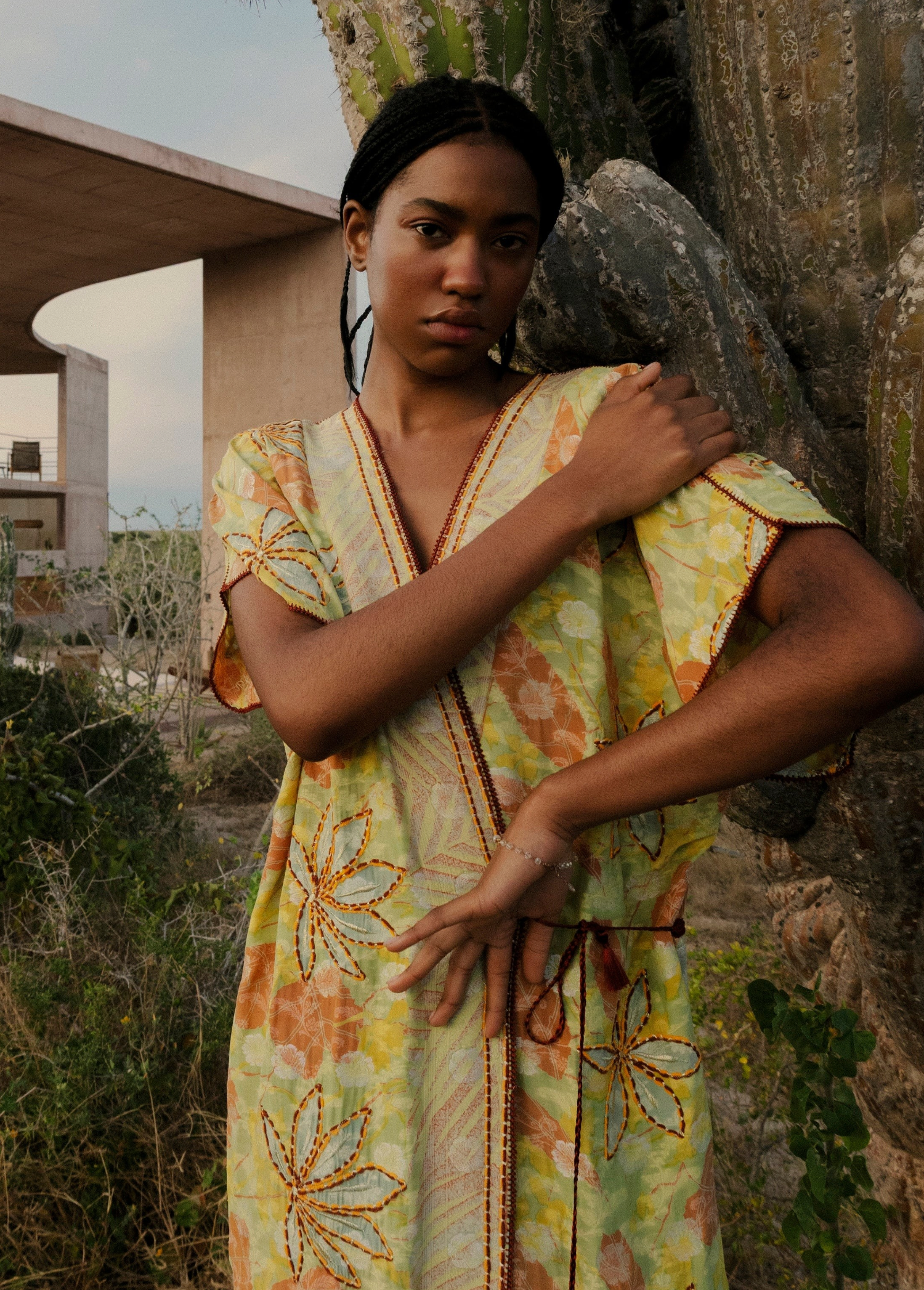 Model wearing a KABE SHOP INC long wrap dress with yellow and green floral sari-inspired embroidery near a cactus.