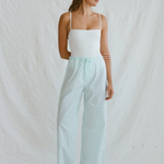 A woman wearing a white camisole and light blue organic cotton Casa Pant wide-leg pants with white sneakers.