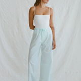 A woman wearing a white camisole and light blue organic cotton Casa Pant wide-leg pants with white sneakers.