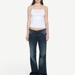 Model wearing a white KABE SHOP INC ribbed cami top with thin straps and pink logo detail, paired with flared jeans.