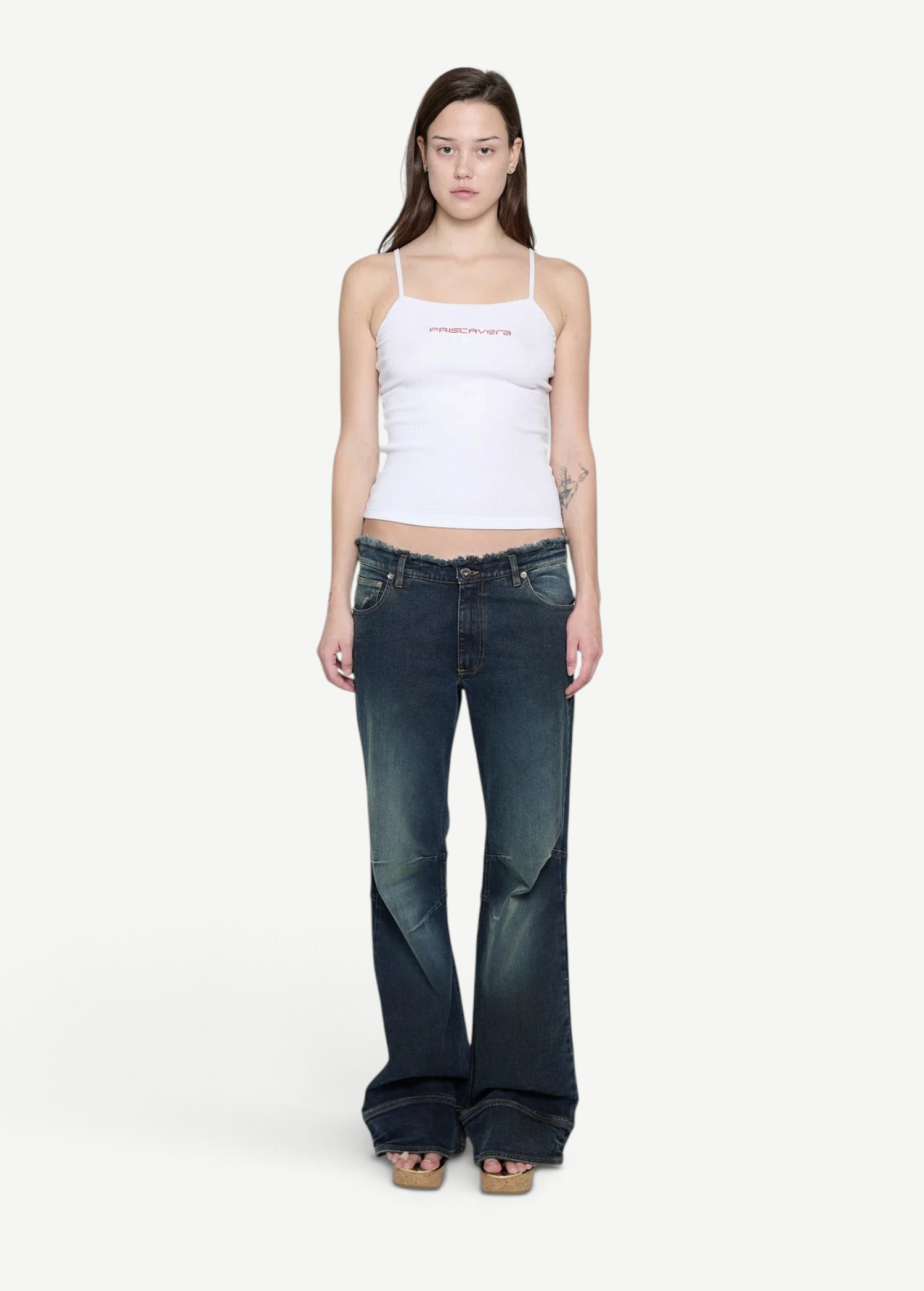 Model wearing a white KABE SHOP INC ribbed cami top with thin straps and pink logo detail, paired with flared jeans.
