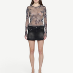 Model wearing a KABE SHOP INC black denim mini skirt with paneled detailing and a long-sleeve patterned mesh top.