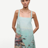A sleeveless light blue Brio Dress featuring a square neckline and a graphic print of a crowded beach scene.