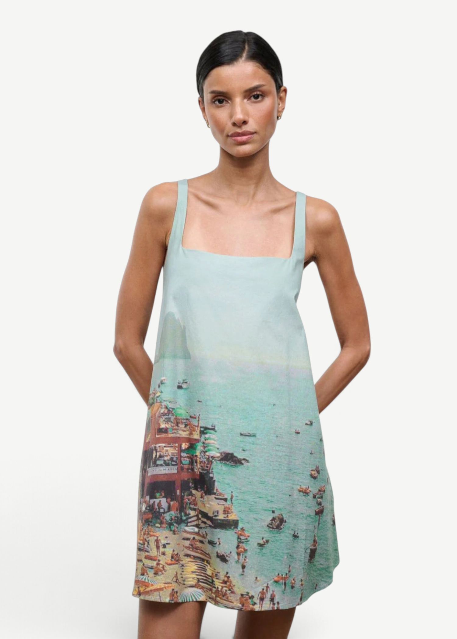 A sleeveless light blue Brio Dress featuring a square neckline and a graphic print of a crowded beach scene.