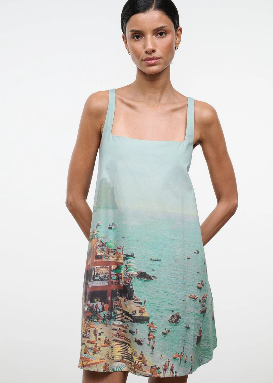 A sleeveless light blue Brio Dress featuring a square neckline and a graphic print of a crowded beach scene.