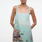 A sleeveless light blue Brio Dress featuring a square neckline and a graphic print of a crowded beach scene.