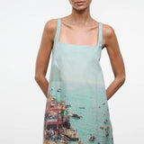 A sleeveless light blue Brio Dress featuring a square neckline and a graphic print of a crowded beach scene.