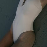 KABE SHOP INC Regatta one piece swimsuit in cream with a modern notched neckline, worn on a sandy beach.