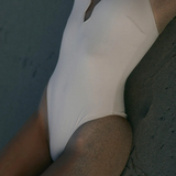 KABE SHOP INC Regatta one piece swimsuit in cream with a modern notched neckline, worn on a sandy beach.