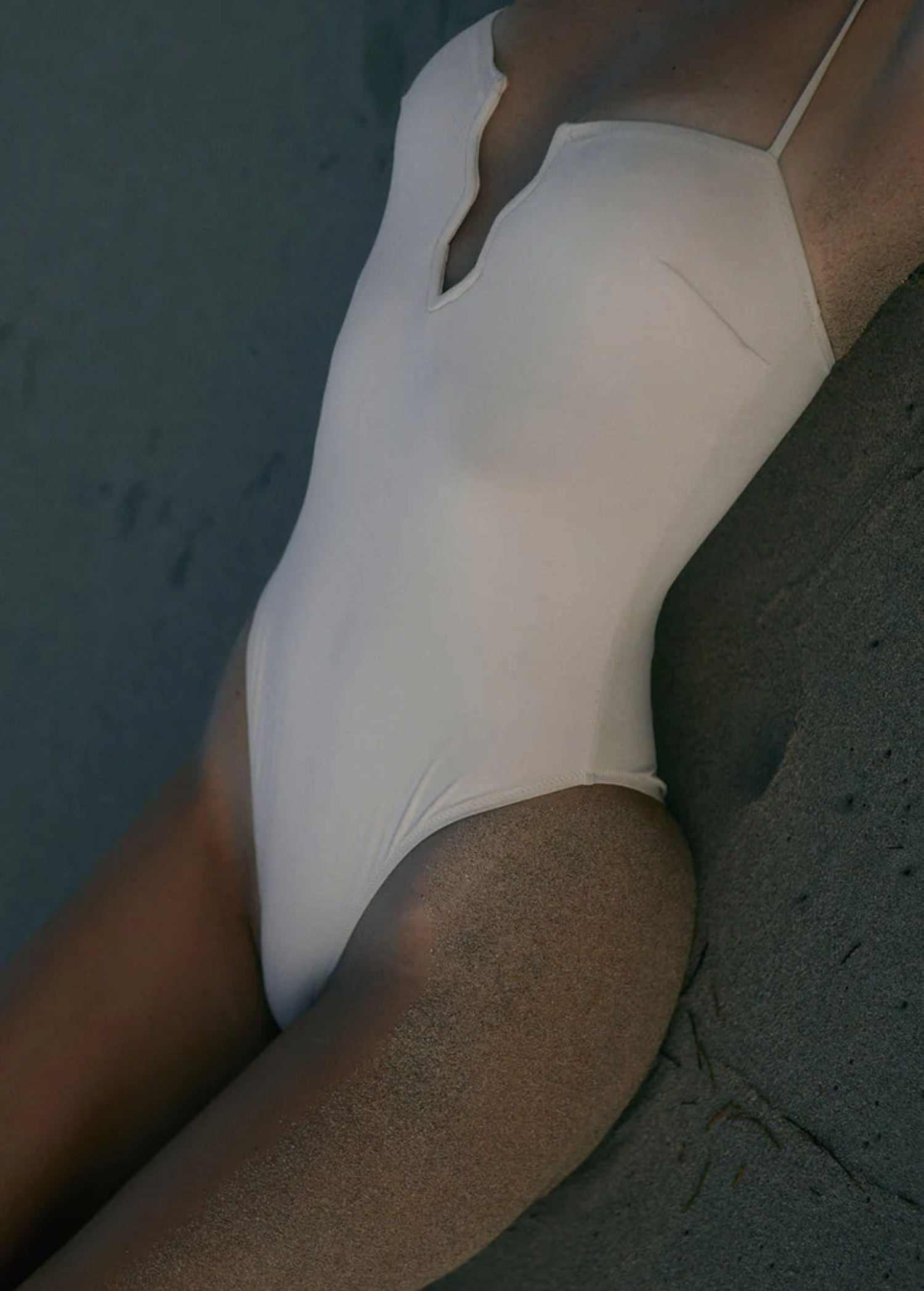 KABE SHOP INC Regatta one piece swimsuit in cream with a modern notched neckline, worn on a sandy beach.