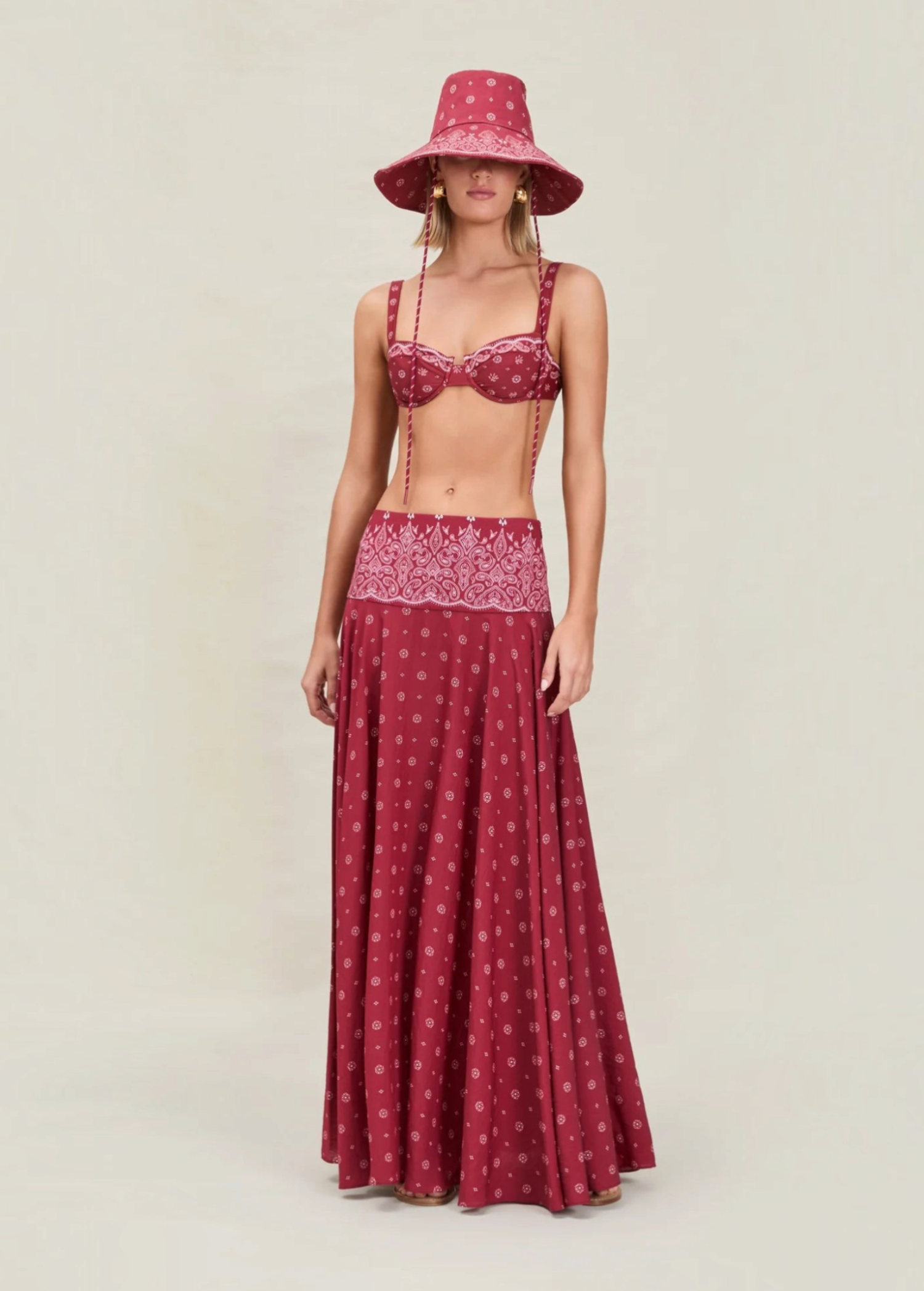 A person wearing a maroon bikini top and matching Rylie Skirt featuring a white floral pattern, styled with a wide-brimmed bucket hat in the same fabric.