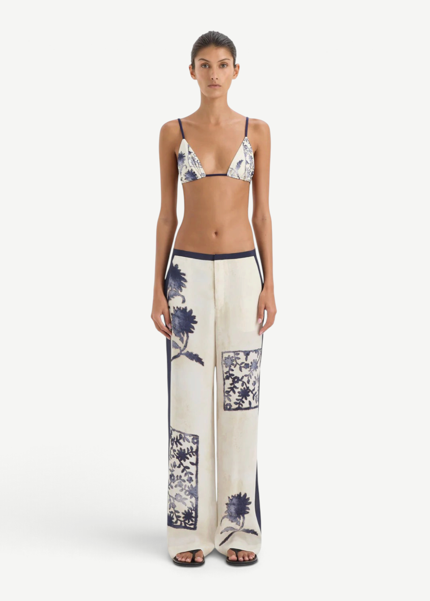 A person wearing a blue and white vintage print bikini top and matching Phillipa Trouser featuring blue side panels.