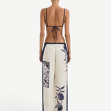Back view of a person wearing a navy blue bikini top and Phillipa Trouser cream-colored wide-leg trousers featuring a vintage floral print.