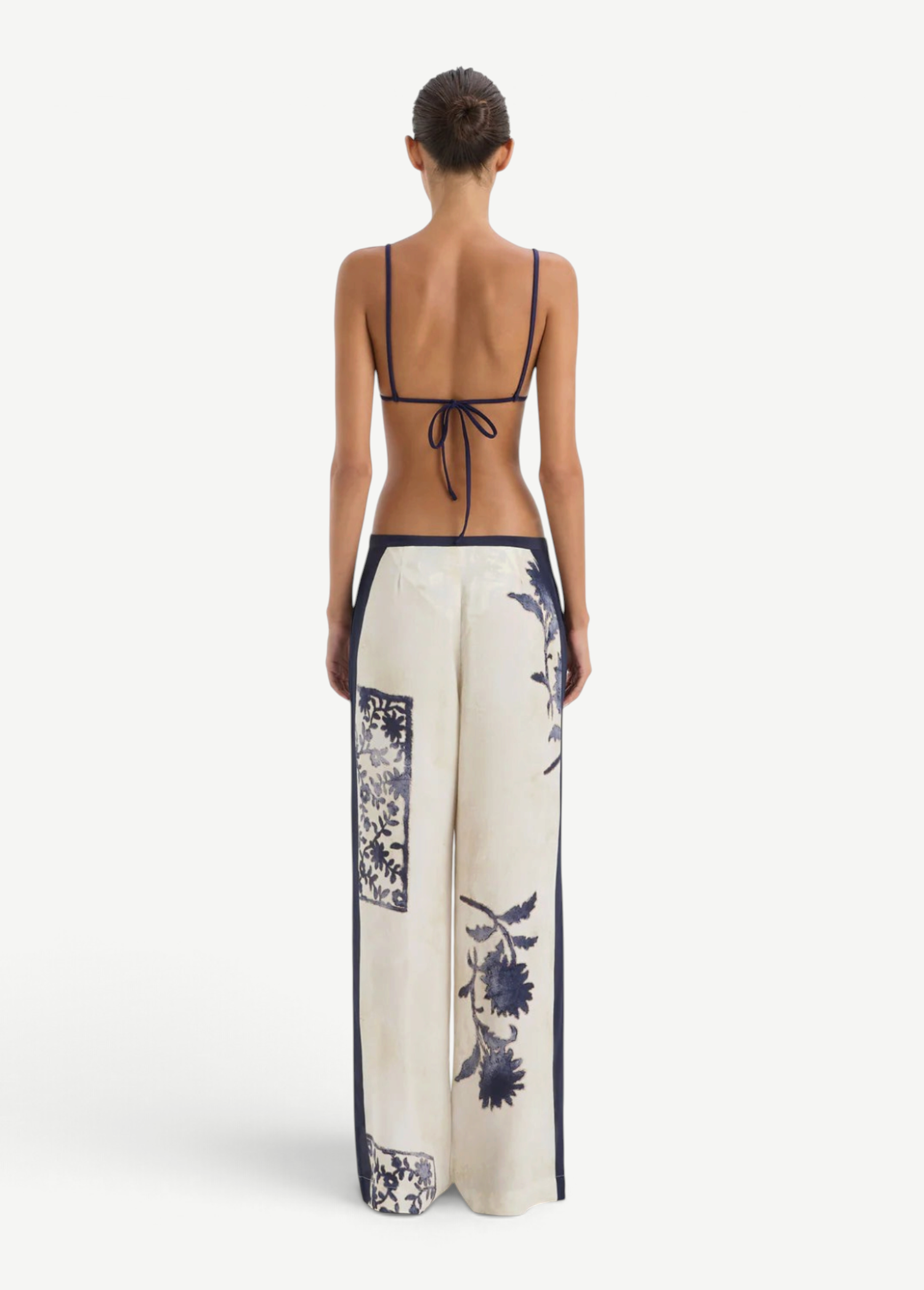 Back view of a person wearing a navy blue bikini top and Phillipa Trouser cream-colored wide-leg trousers featuring a vintage floral print.
