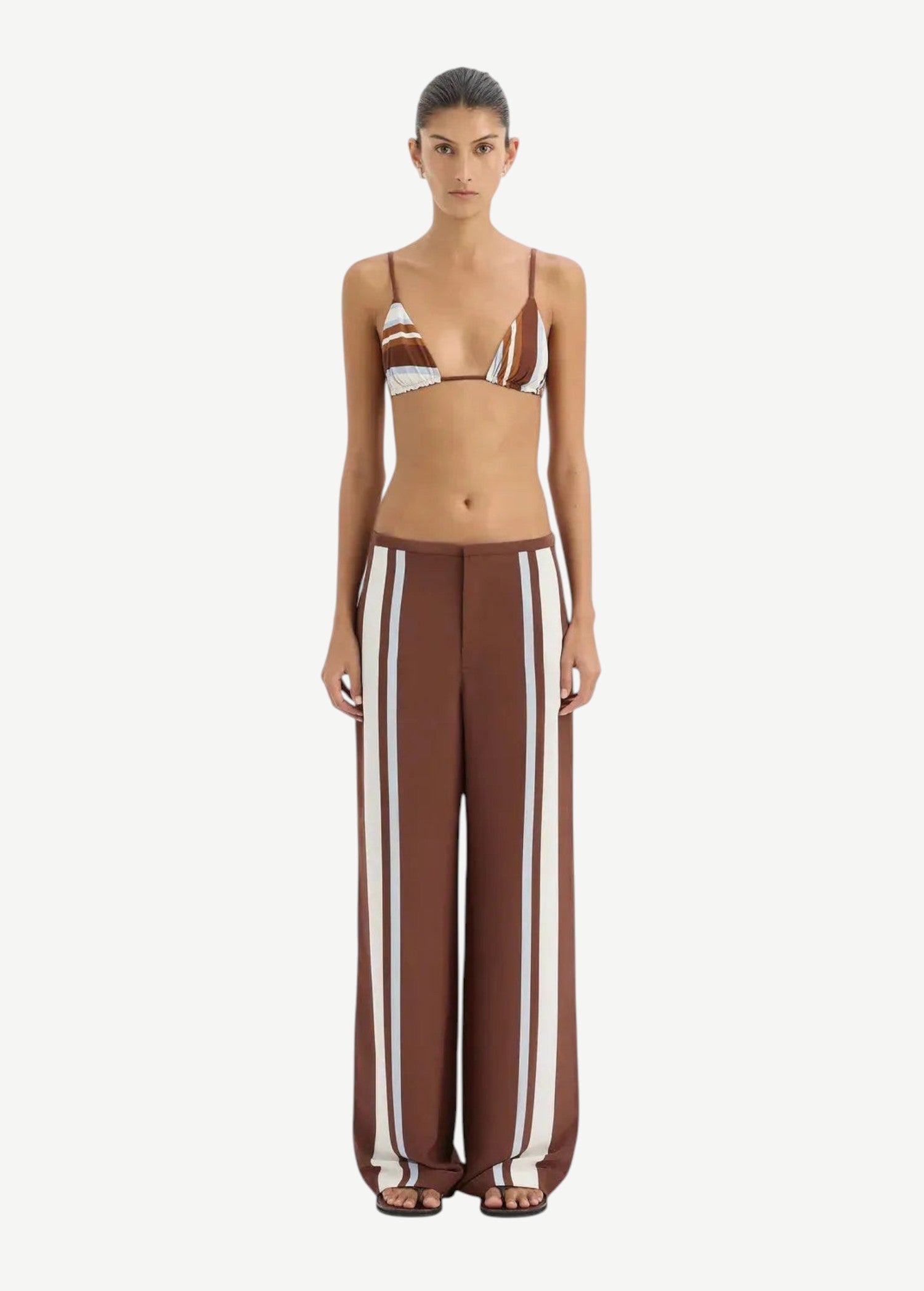 Woman wearing a brown and white striped bikini with matching pants on a white background.