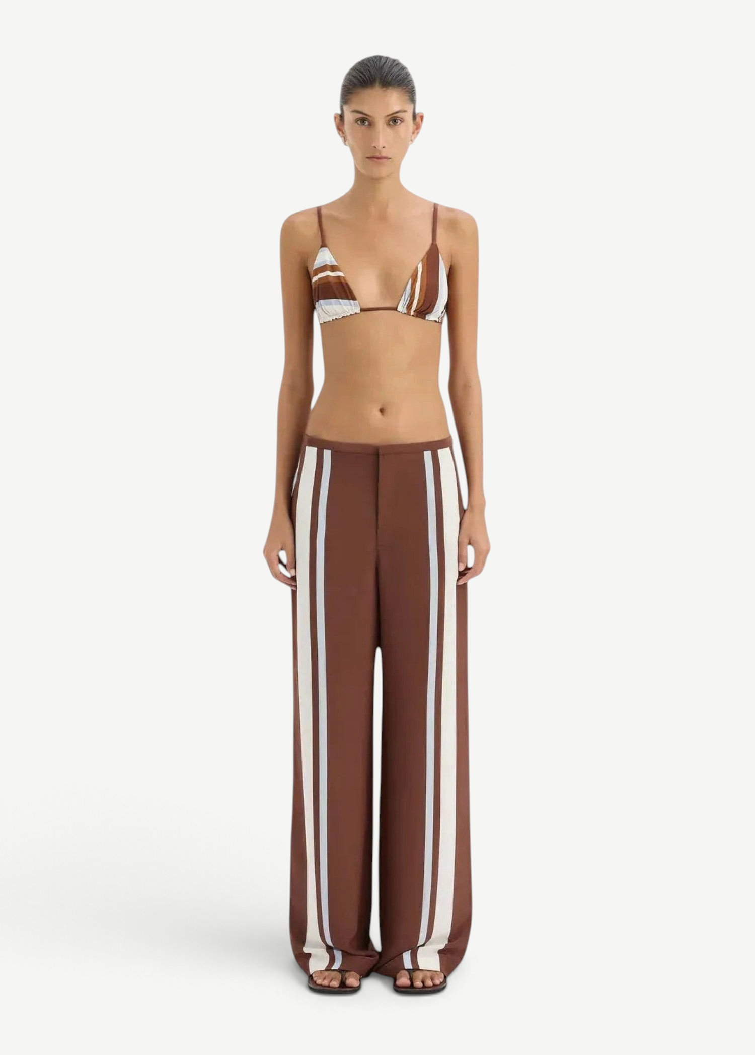 Woman wearing a brown and white striped bikini with matching pants on a white background.