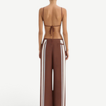 A person seen from behind wears the Marais Trouser, matte crepe wide-leg trousers with vertical white stripes down the sides, paired with a matching brown string top.