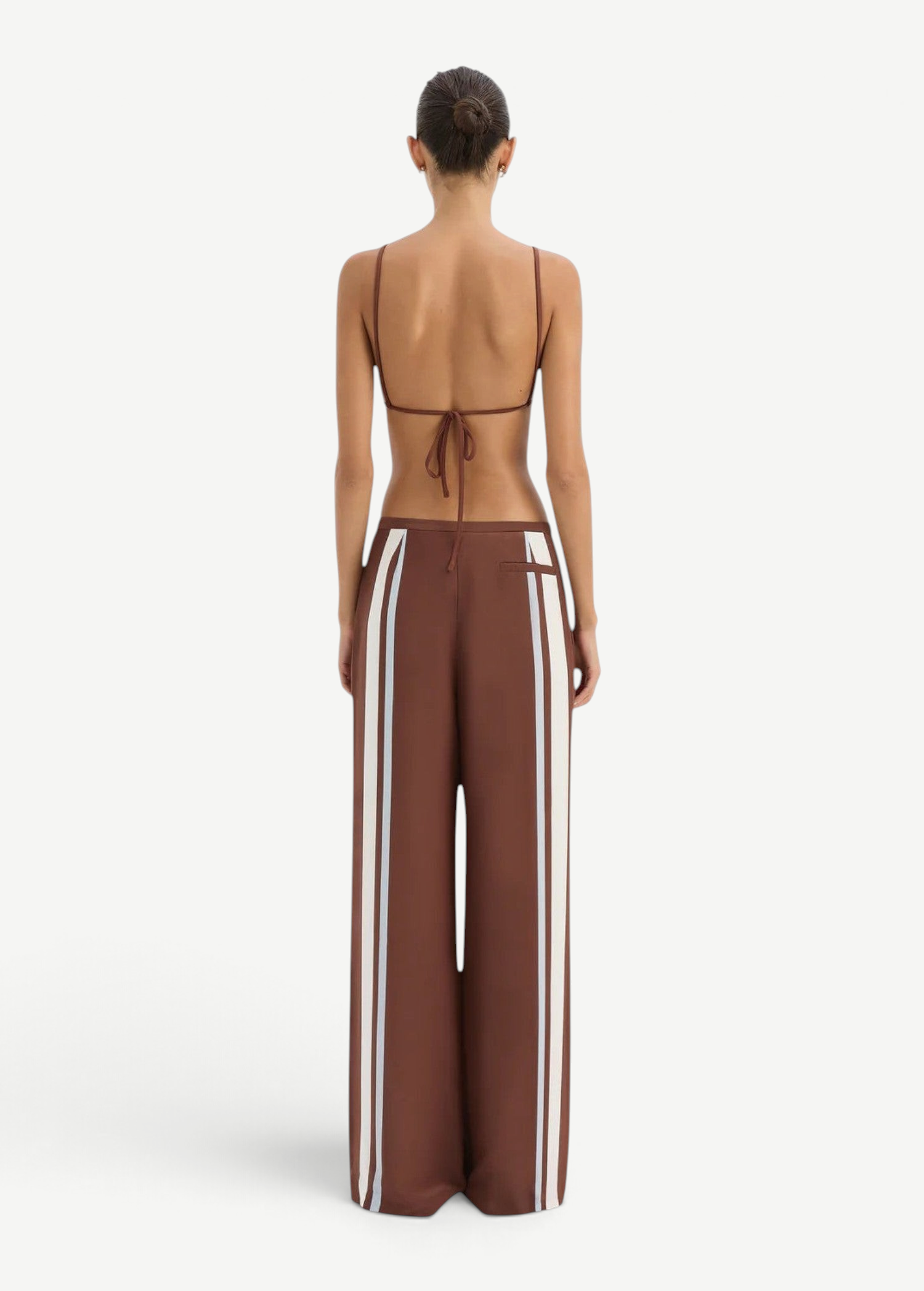 A person seen from behind wears the Marais Trouser, matte crepe wide-leg trousers with vertical white stripes down the sides, paired with a matching brown string top.
