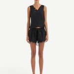 A person wearing the Klara Mini Short, featuring a black sleeveless top with asymmetrical floral cut-out embroidery and matching shorts with a scalloped hem and tie waistband.