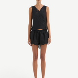 A person wearing the Klara Mini Short, featuring a black sleeveless top with asymmetrical floral cut-out embroidery and matching shorts with a scalloped hem and tie waistband.
