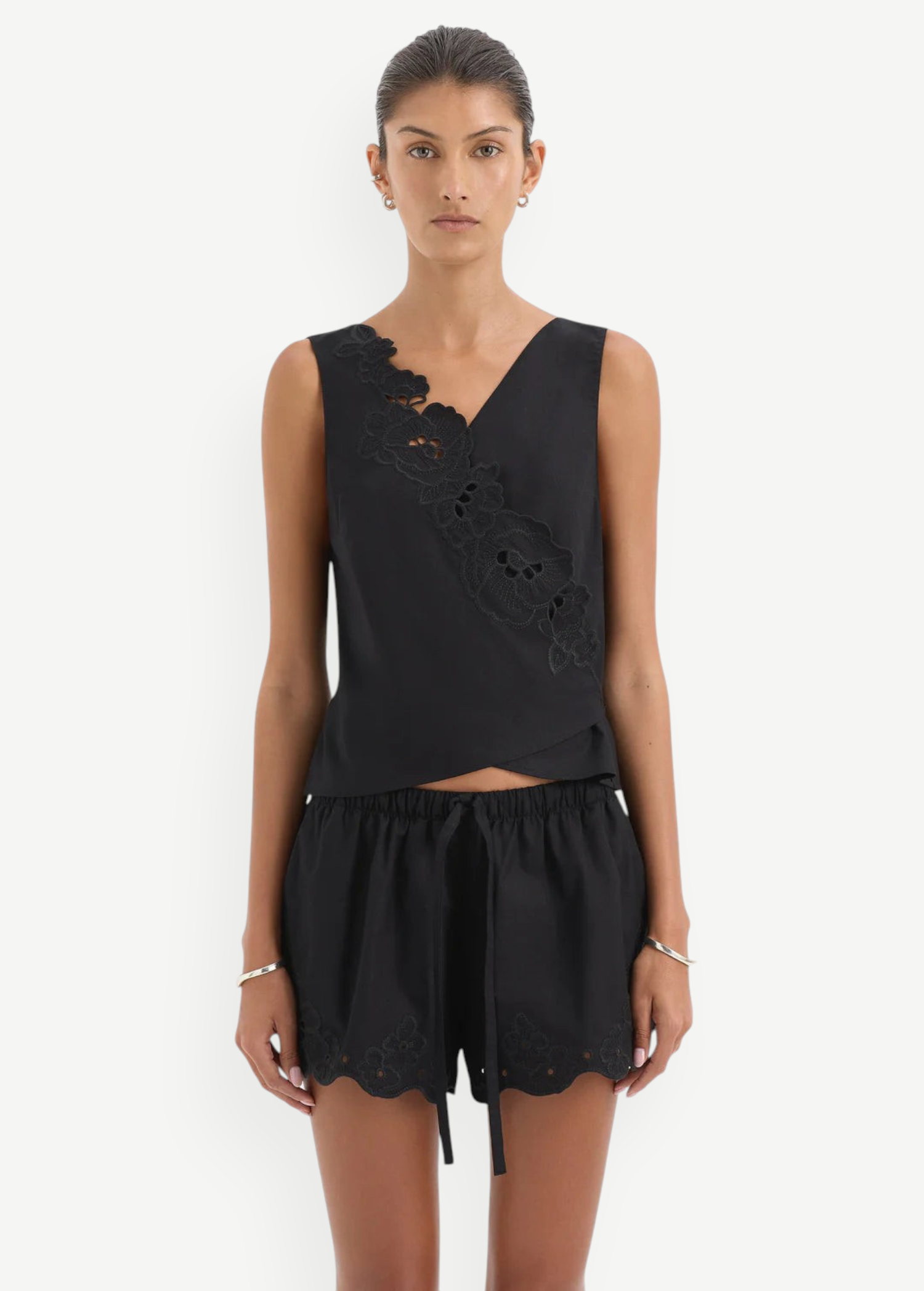 Klara Mini Short featuring a black sleeveless top with an asymmetrical floral cut-out embroidery overlay and matching black drawstring shorts with a scalloped hem and a tie waistband.
