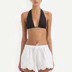 A person wearing a black halter-neck bikini top and Klara Mini Short white drawstring shorts featuring floral cut-out embroidery and a scalloped hem.