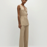 A woman wears a beige Selan Top, a sleeveless V-neck tunic with a drawstring waist, paired with matching pinstripe wide-leg trousers.
