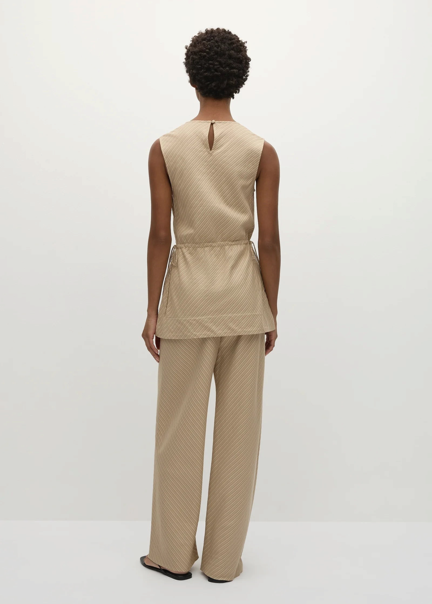Back view of a person in a Selan Top with a cinched waist and matching wide-leg trousers, both featuring a diagonal pinstripe pattern for a refined, relaxed silhouette.