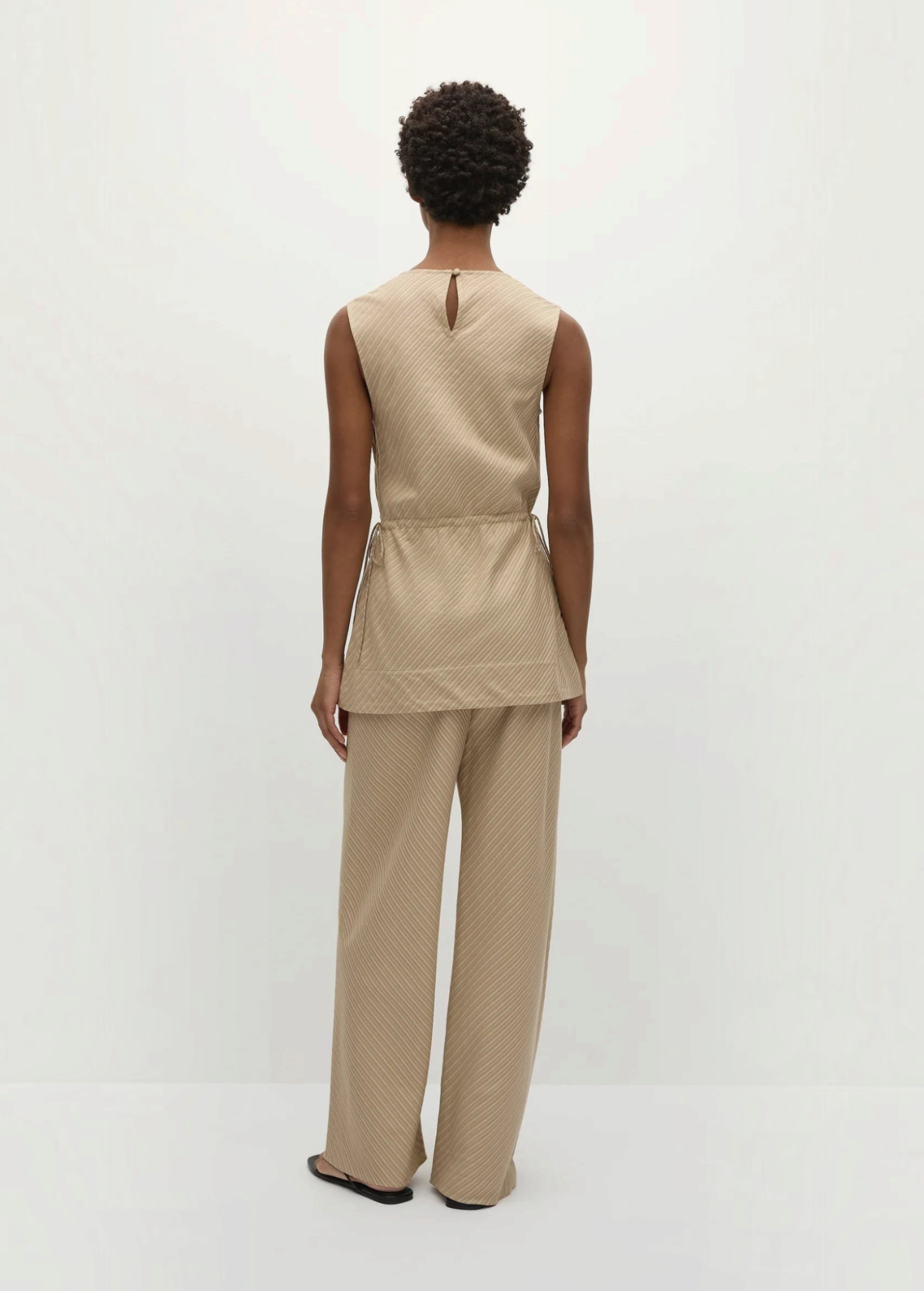 Back view of a person in a Selan Top with a cinched waist and matching wide-leg trousers, both featuring a diagonal pinstripe pattern for a refined, relaxed silhouette.