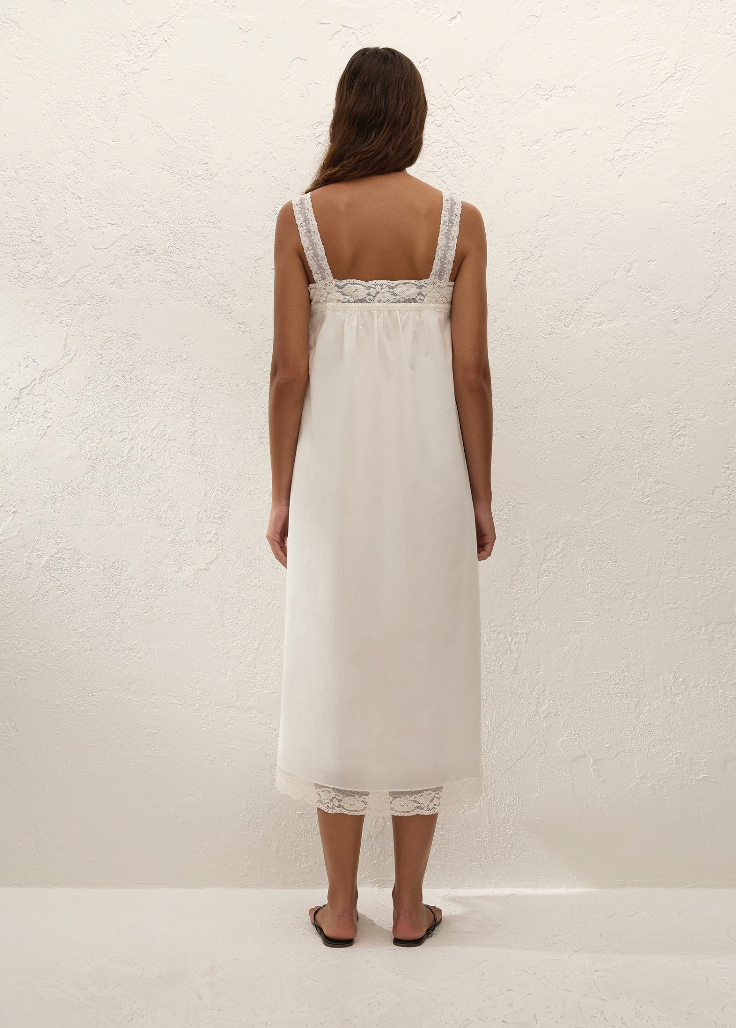 Back view of a woman wearing a white KABE SHOP INC Cristina midi slip dress with delicate lace trim and straps.