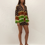 A woman wears a Cora Shirt and matching shorts featuring a pattern of brown, green, and white stripes and geometric shapes.