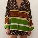 A person wearing a loose-fitting Cora Shirt and matching shorts featuring a brown and green geometric pattern with horizontal stripes.