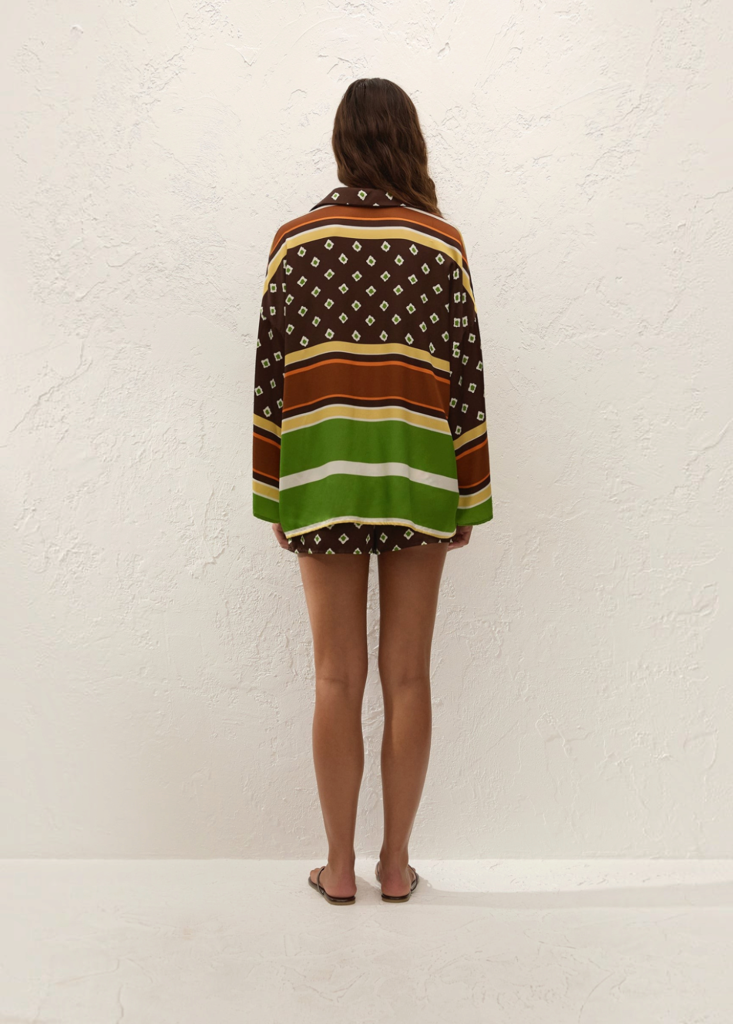 A person viewed from behind wearing a vacation-ready Cora Shirt and matching shorts in a geometric and striped pattern of brown, green, and white.