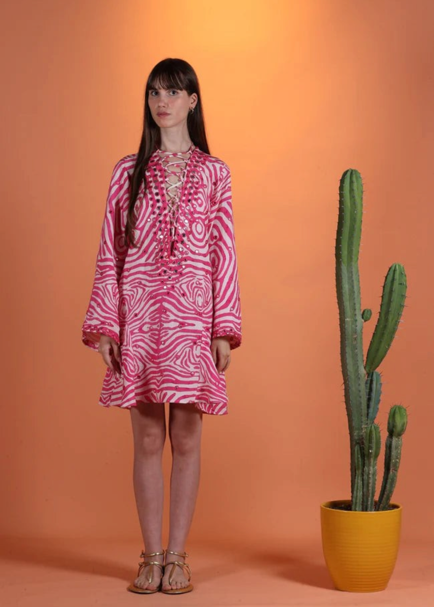 Model wearing a KABE SHOP INC Poccaa pink and white zebra print short kaftan with lace-up neckline and mirror details.