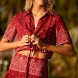 A person wearing a Rosie Top, a short-sleeved, button-down cropped shirt with an adjustable drawstring waist in a red and white paisley print.