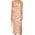 Woman wearing the Chloe One Shoulder Midi Dress, featuring a white, one-shoulder design with orange and red floral prints. The dress is crafted from lightweight linen and fully lined for comfort. She holds a small handbag and wears sandals, standing facing forward against a plain white background.