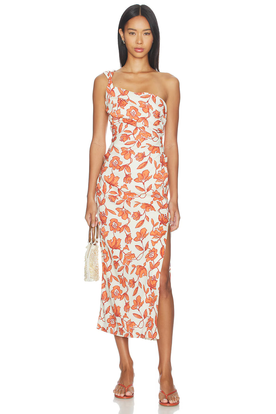 A woman models the Chloe One Shoulder Midi Dress—a sleeveless, one-shoulder white midi dress featuring a bold orange floral print, side slit, and crafted from lightweight linen fabric made in Turkey. The fully lined dress is styled with flat sandals and a small woven handbag as she stands against a white background.