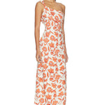 A woman models the Chloe One Shoulder Midi Dress—an ankle-length, white dress featuring an orange floral pattern, crafted from lightweight linen and fully lined for comfort. She pairs it with flat sandals and stands against a plain white background.