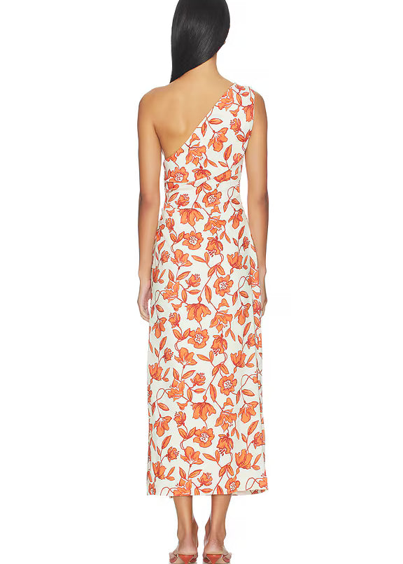 A woman with long dark hair, seen from behind, stands barefoot against a white background wearing the Chloe One Shoulder Midi Dress—a white linen midi dress with an orange floral print. Crafted in Turkey from lightweight, fully lined linen for comfort.