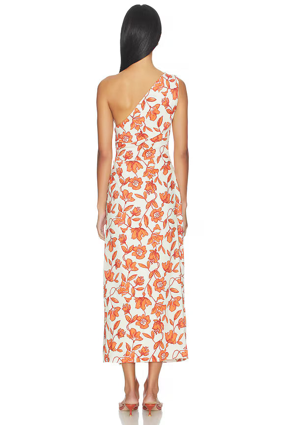 A woman with long dark hair, seen from behind, stands barefoot against a white background wearing the Chloe One Shoulder Midi Dress—a white linen midi dress with an orange floral print. Crafted in Turkey from lightweight, fully lined linen for comfort.