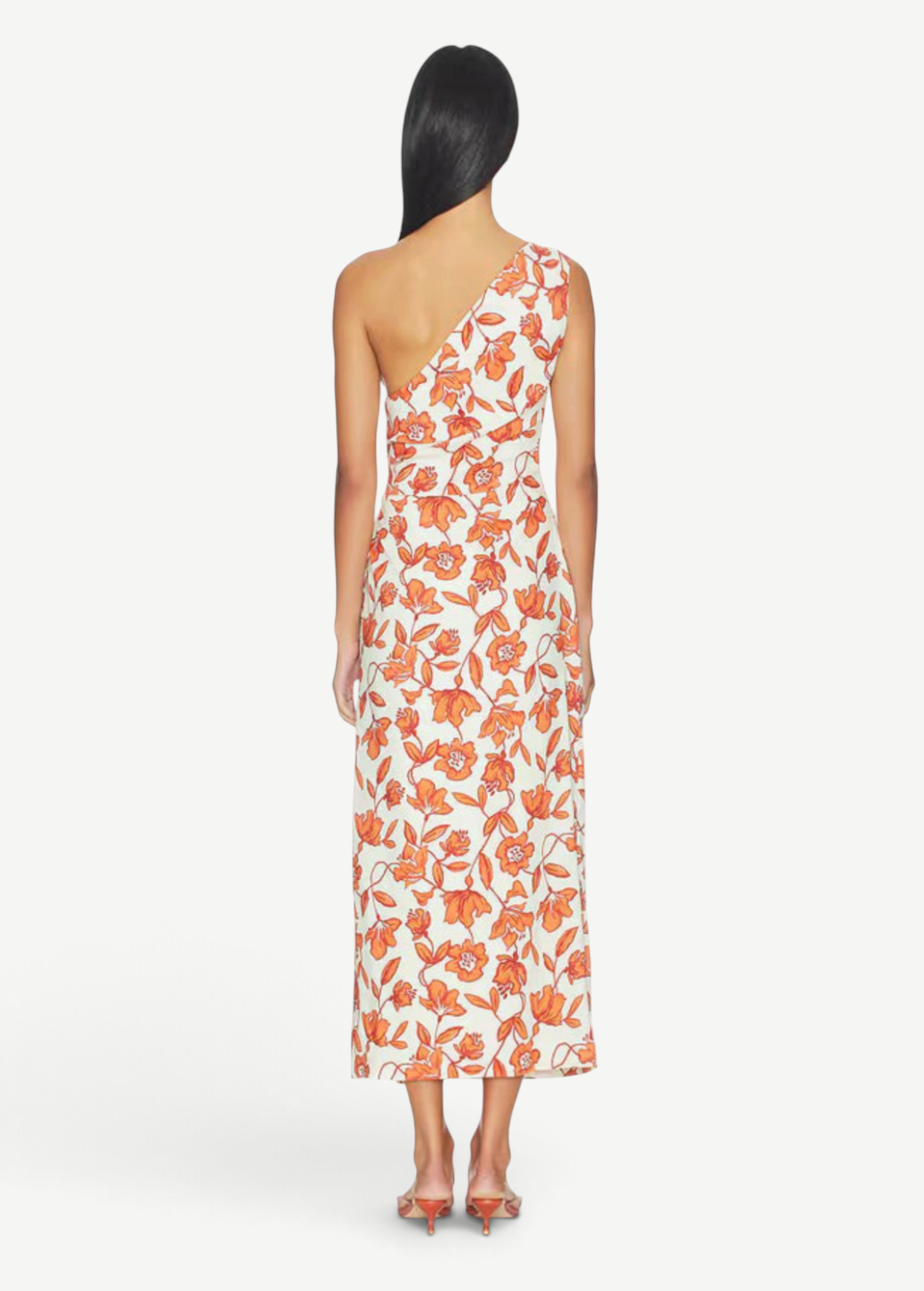 A woman with long dark hair, seen from behind, stands barefoot against a white background wearing the Chloe One Shoulder Midi Dress—a white linen midi dress with an orange floral print. Crafted in Turkey from lightweight, fully lined linen for comfort.