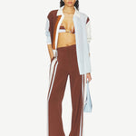 A person wearing Marais Trouser wide-leg silk trousers with white side stripes, an unbuttoned color-blocked shirt, and a striped bikini top.
