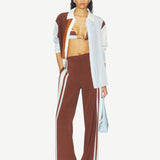 A person wearing Marais Trouser wide-leg silk trousers with white side stripes, an unbuttoned color-blocked shirt, and a striped bikini top.