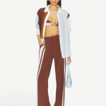 A person wearing Marais Trouser wide-leg silk trousers with white side stripes, an unbuttoned color-blocked shirt, and a striped bikini top.