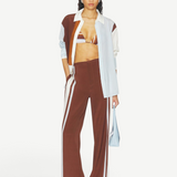 A person wearing Marais Trouser wide-leg silk trousers with white side stripes, an unbuttoned color-blocked shirt, and a striped bikini top.