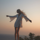 Model wearing a white KABE SHOP INC Thaleen Mini Kaftan with flared sleeves at sunset by the ocean.
